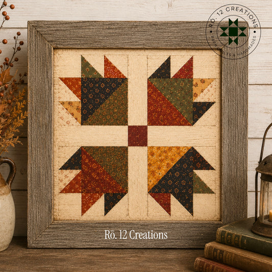 A framed quilt pattern featuring a rustic four-quilt block design with geometric patches in earthy tones of rust red, olive green, mustard yellow, and navy blue on a cream background. The frame is weathered gray wood.