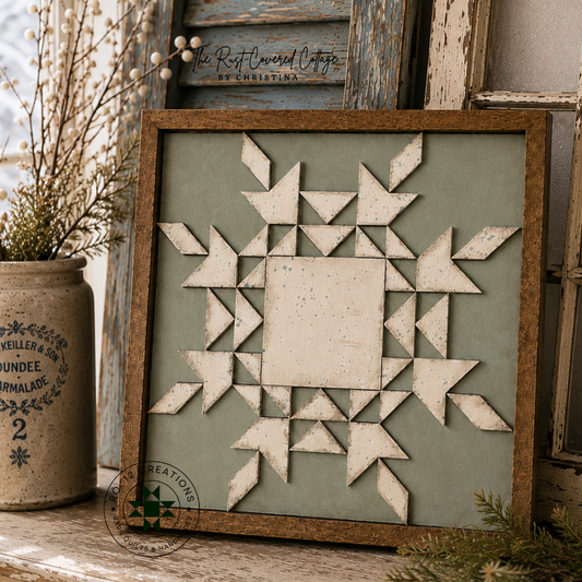 A rustic framed quilted wall art piece featuring a geometric snowflake design, styled on a distressed wooden cabinet with a vintage mason jar and weathered shutters in the background.
