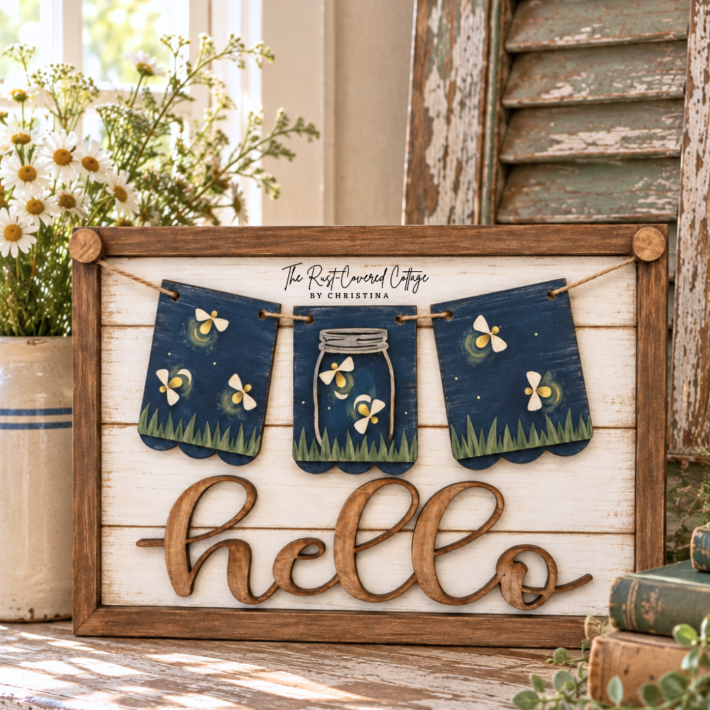 Finished Fireflies interchangeable banner featuring fireflies and a mason jar on a rustic Hello sign base, styled with vintage books, greenery, white flowers, and aged cottage décor.
