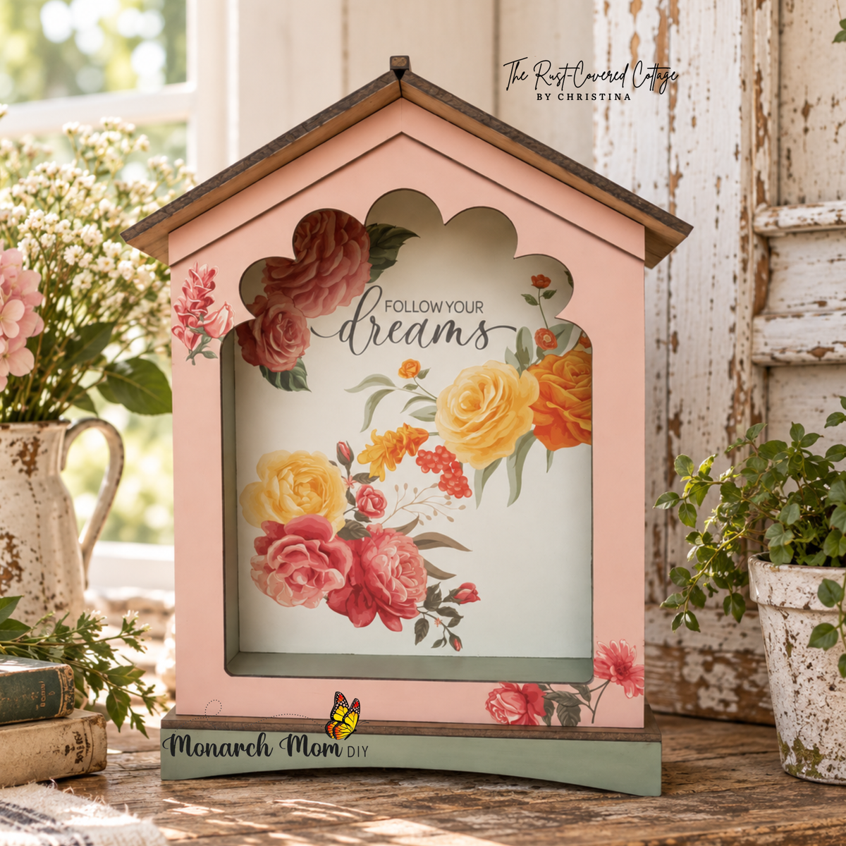 Floral house-shaped sign with “Follow Your Dreams” lettering displayed on worn wood with chippy white architectural accents and soft natural light.